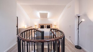 A modern bedroom with a central bed, a staircase, and a floor lamp.