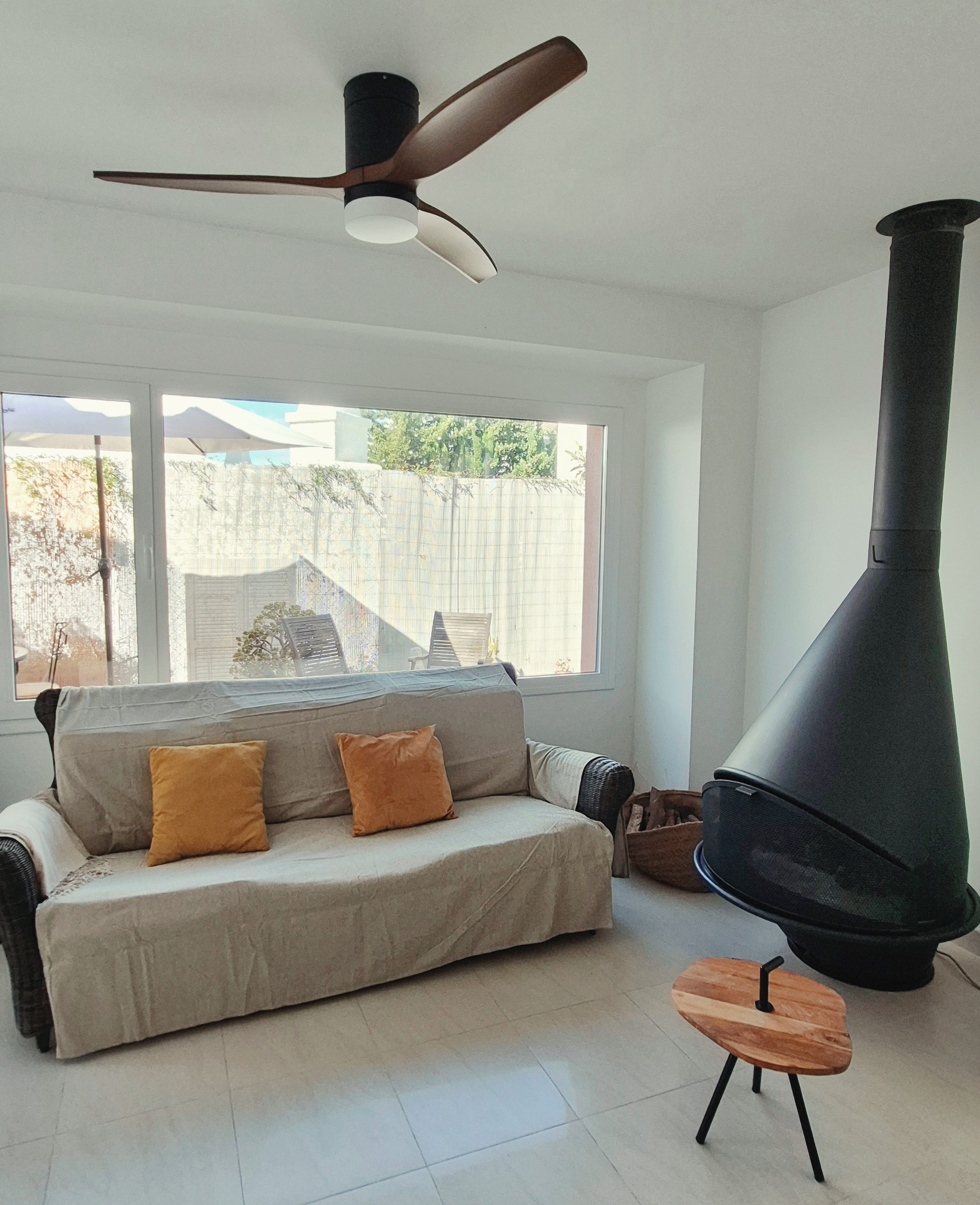 Un salon moderne avec un canapé, une petite table, une grande cheminée et un ventilateur de plafond.