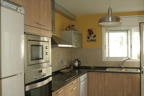 A kitchen with stainless steel appliances, wooden cabinets, a window, and a wall-mounted light fixture. - Nice villa with wonderful sights, come to profite sunrise on the ser (Torredembarra)
