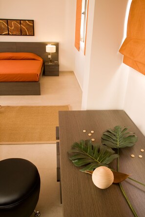 A modern hotel room with a bed, bedside table, lamp, and a decorative plant.