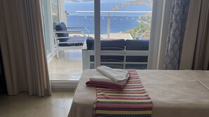 Una camera d'hotel con un balcone, un letto con una coperta a righe colorate e vista sul mare e sulle montagne.