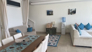 A modern living room with a dining area, featuring a sofa, a coffee table, and a water dispenser. - Apartment With Shared Pool And Sea Views (Kalkan)