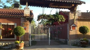 A gated entrance to a building with a tiled roof, a brick wall, and a metal gate. There are potted plants outside the gate.
