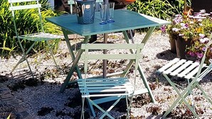 An outdoor patio with a table and chairs, a green umbrella, and a mural of a parrot on the wall. - Beautiful, spacious, 2 bed renovated breton cider press, 10km from the coast! (Cast)