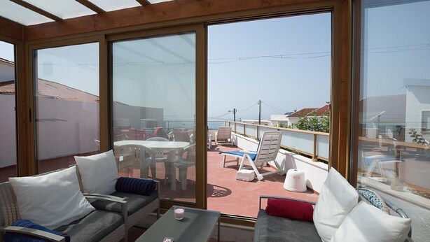 Ein sonnendurchfluteter Raum mit einem großen Glasbalkon zur Terrasse. Im Inneren befinden sich zwei Sofas und ein kleiner Tisch.