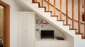 Eine Treppe mit Holzspindeln führt zu einer Zwischenebene mit einem weißen Schrank und einem Flachbildfernseher.