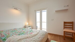 Ein Schlafzimmer mit Bett, Stuhl, Nachttisch, Fenster und Deckenleuchte.