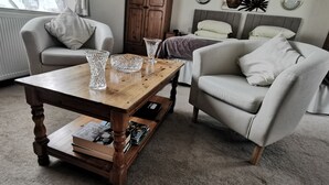 A cozy living room with a wooden coffee table, two armchairs, a bookshelf, and a radiator. - Fantastic self-catering apartment on the outskirts of Caerleon (Caerleon)