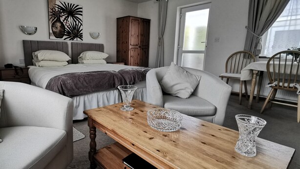 A modern bedroom with a large bed, two sofas, a wooden coffee table, and a dining area with chairs. - Fantastic self-catering apartment on the outskirts of Caerleon (Caerleon)
