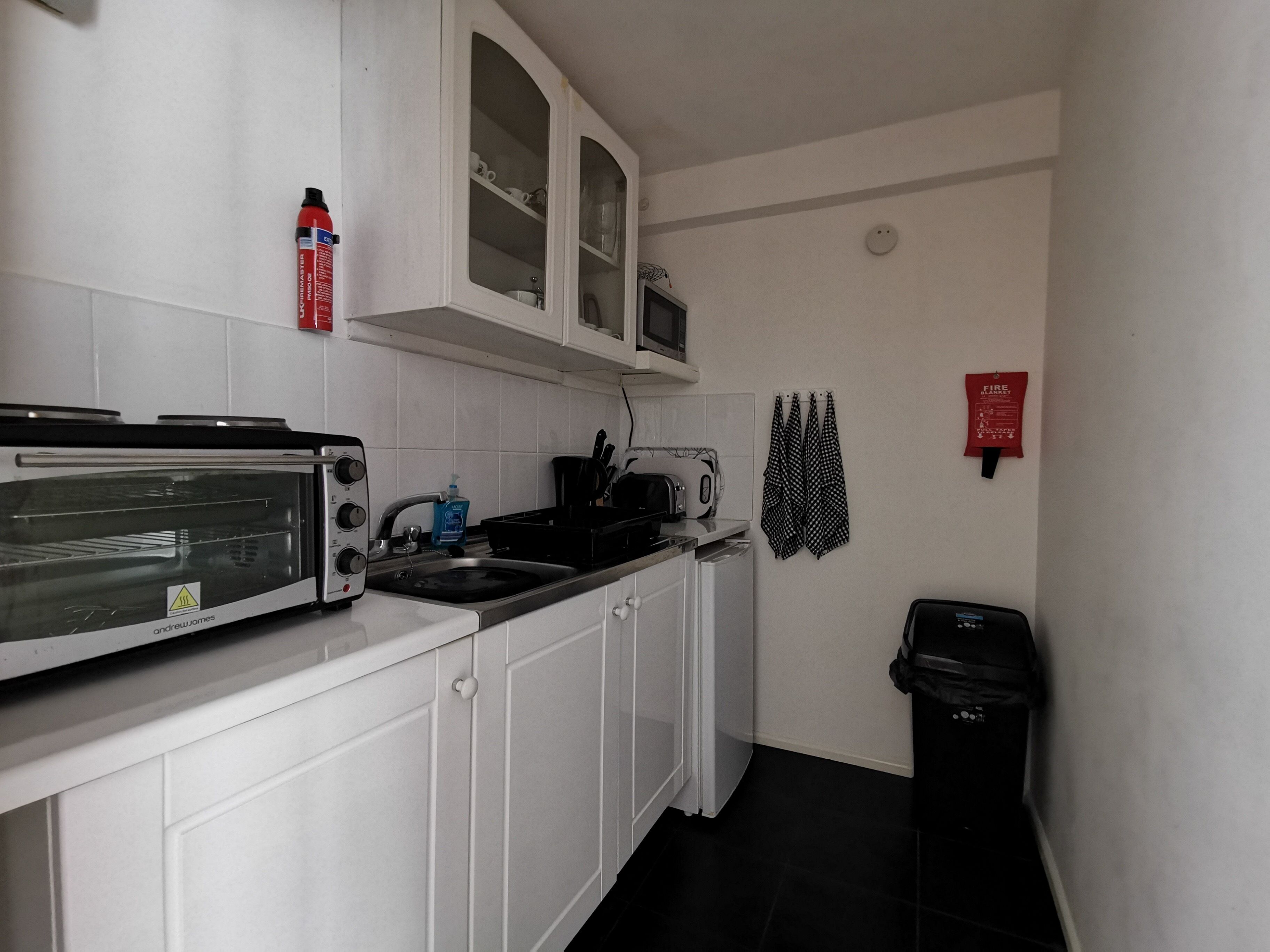 A compact kitchen with white cabinets, a built-in microwave, a toaster, and a sink.
