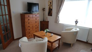 A living room with a wooden cabinet, a television on top, a table with a vase, two chairs, and a window with curtains. - Fantastic self-catering apartment on the outskirts of Caerleon (Caerleon)