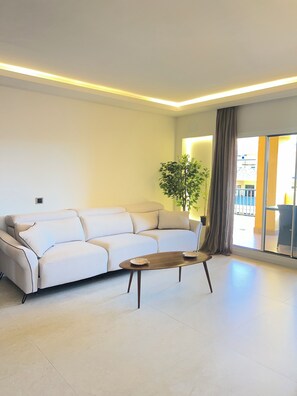Una sala moderna con un sofá, una mesa de centro, una planta y vistas a través de una puerta de cristal.