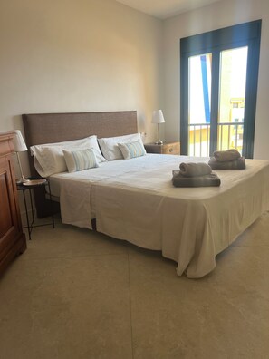 Habitación de hotel con una cama grande, una mesita de noche, una lámpara y vistas al exterior.