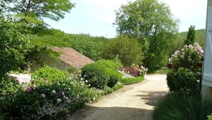 A gravel path flanked by lush greenery and flowering plants, leading to a stone building with a sloped roof. - Charming authentic cosy cottage in the heart of the Quercy countryside (Mauroux)