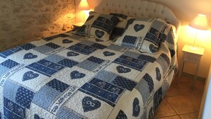 A bed with a quilted headboard, two bedside lamps, and a stone wall. - Charming authentic cosy cottage in the heart of the Quercy countryside (Mauroux)