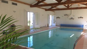 An indoor swimming pool with wooden beams, a tiled deck, and a view of the outside. - Charming authentic cosy cottage in the heart of the Quercy countryside (Mauroux)