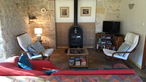 A cozy living room with a stone wall, a fireplace, two armchairs, a sofa, a coffee table, and a bookshelf. - Charming authentic cosy cottage in the heart of the Quercy countryside (Mauroux)