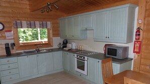 A compact kitchen with light blue cabinets, a built-in oven, a microwave, and a window with a view of greenery.