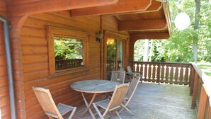 A wooden deck with a round table and four chairs, a railing, and a view of greenery.