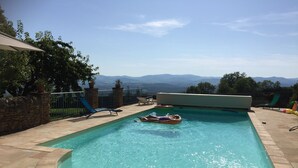 Ein Pool mit gewölbter Kante, umgeben von Steinfliesen. Liegestühle und Blick auf ferne Berge.