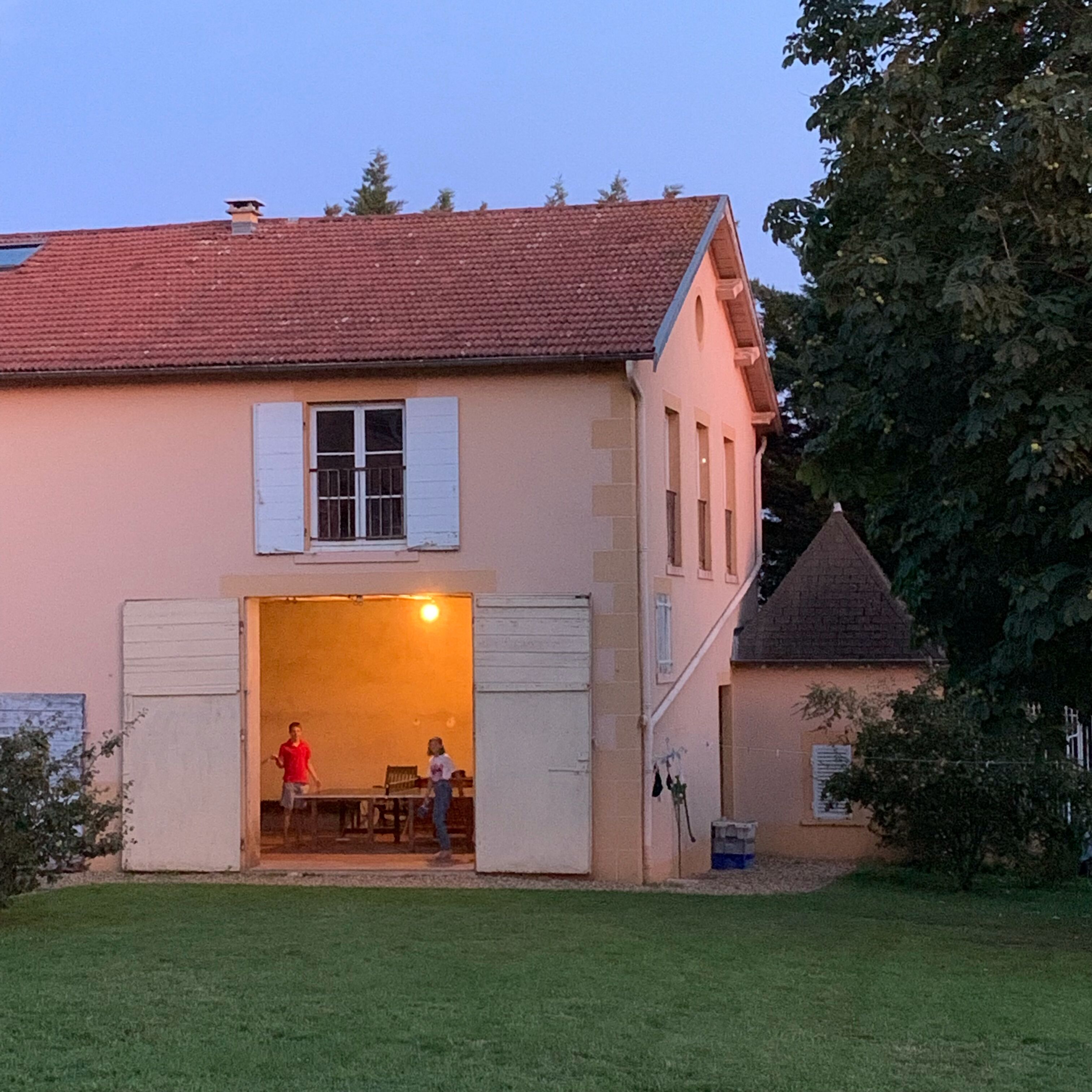 A two-story house with a red-tiled roof and a garage door open.