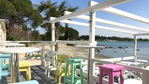 Een terras met kleurrijke stoelen en tafels, met uitzicht op een waterpartij en een strand.