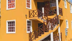 A yellow building with a staircase and multiple windows. - Frontline apartment No. 2 (Oistins)