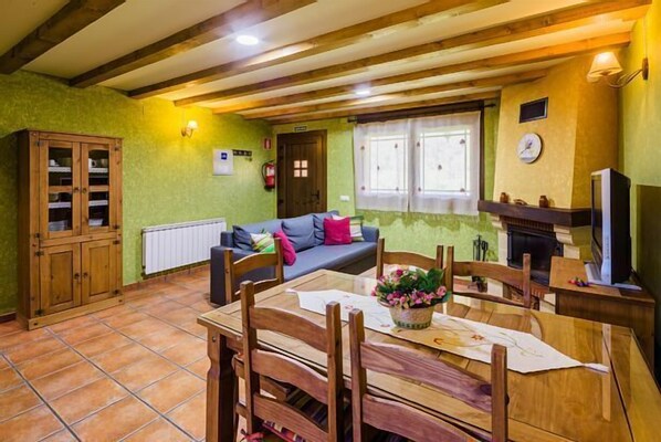 A cozy living room with a wooden dining table, a sofa, and a fireplace. - Rural apartment L'Abiseu for 4 people (Villablino)