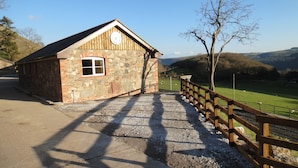 A stone building with a clock, a gravel path, and a wooden fence overlooking a green field.