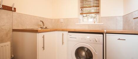 A compact kitchen with a built-in washing machine, a window with blinds, and a radiator.