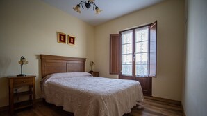A bedroom with a wooden bed, a nightstand, a lamp, and a window with curtains. - Apartamentos Jesús for 4 people (Valdés)
