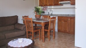 A compact kitchen with wooden cabinets, a dining table with chairs, a microwave, and a clock on the wall. - Apartamentos Jesús for 4 people (Valdés)