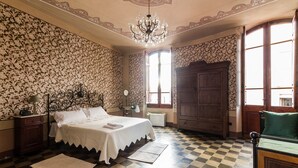 A bedroom with a checkered floor, a large bed with a white bedspread, a wooden wardrobe, and a chandelier. - fully frescoed home in Sardinia (Quartu Sant'Elena)