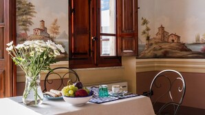 A dining area with a table set for two, a vase of flowers, and a painting on the wall. - fully frescoed home in Sardinia (Quartu Sant'Elena)