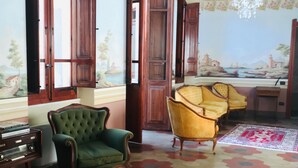 A room with hexagonal patterned flooring, a green armchair, a yellow armchair, and wooden doors with open shutters. - fully frescoed home in Sardinia (Quartu Sant'Elena)