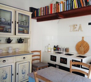 A kitchen with white cabinets, a wooden table, and a shelf with books. - fully frescoed home in Sardinia (Quartu Sant'Elena)