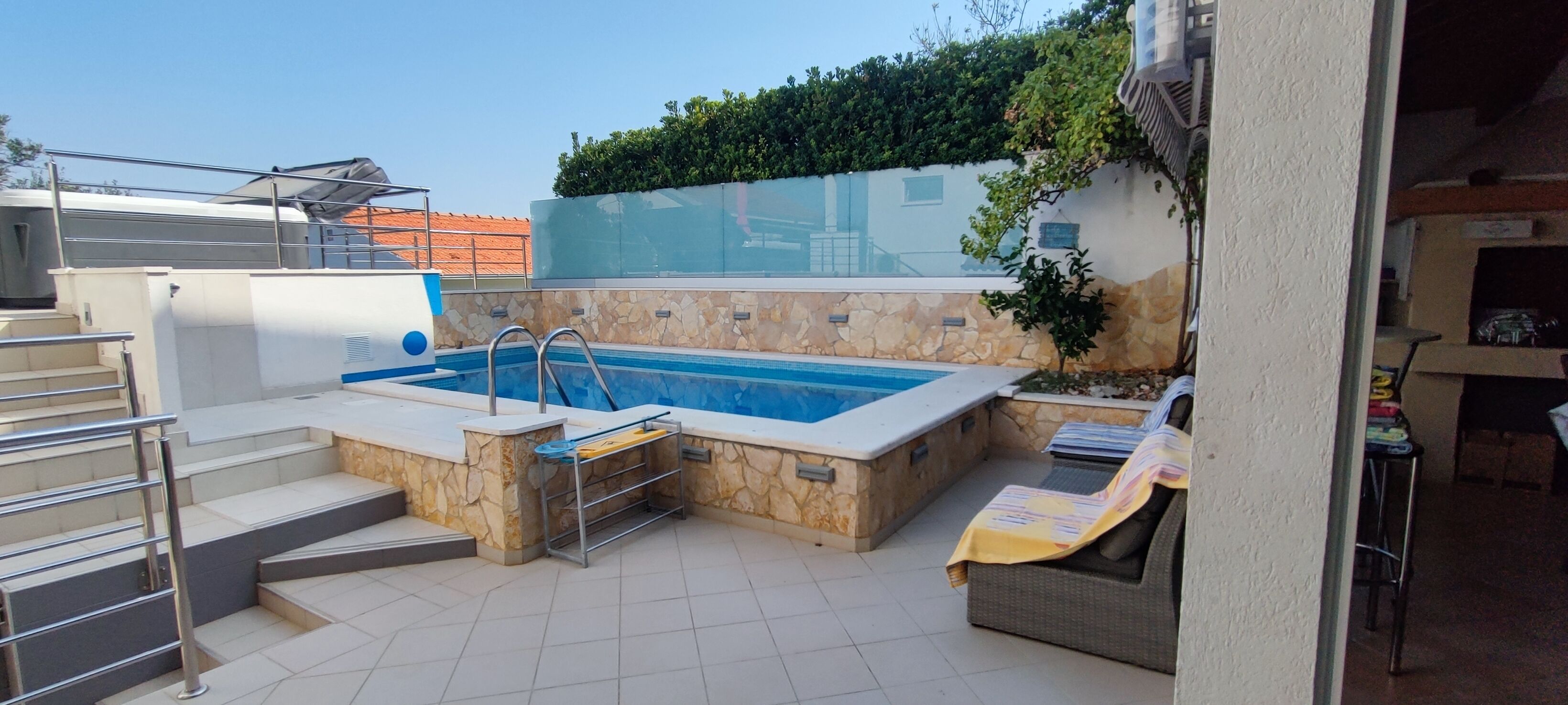 A rooftop swimming pool with a stone wall, a hot tub, and a covered seating area.
