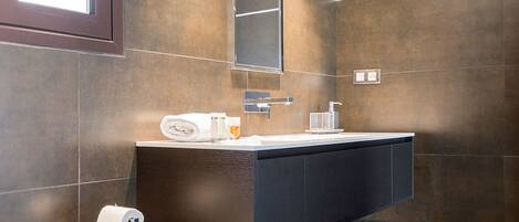 A modern bathroom with a dark brown tiled wall, a large mirror, a white sink, and a toilet.