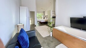 A modern living room with a black leather sofa, a flat-screen TV, and a large window. - Spacious 3-Level Loft: Functionality & Comfort for Long-Term Stays (Santa Ana)