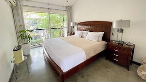 A hotel room with a large bed, a nightstand with a lamp, a potted plant, and a view of greenery outside. - Spacious 3-Level Loft: Functionality & Comfort for Long-Term Stays (Santa Ana)