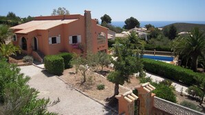 Una villa in stile mediterraneo con facciata in pietra, una piscina e vista sul mare.