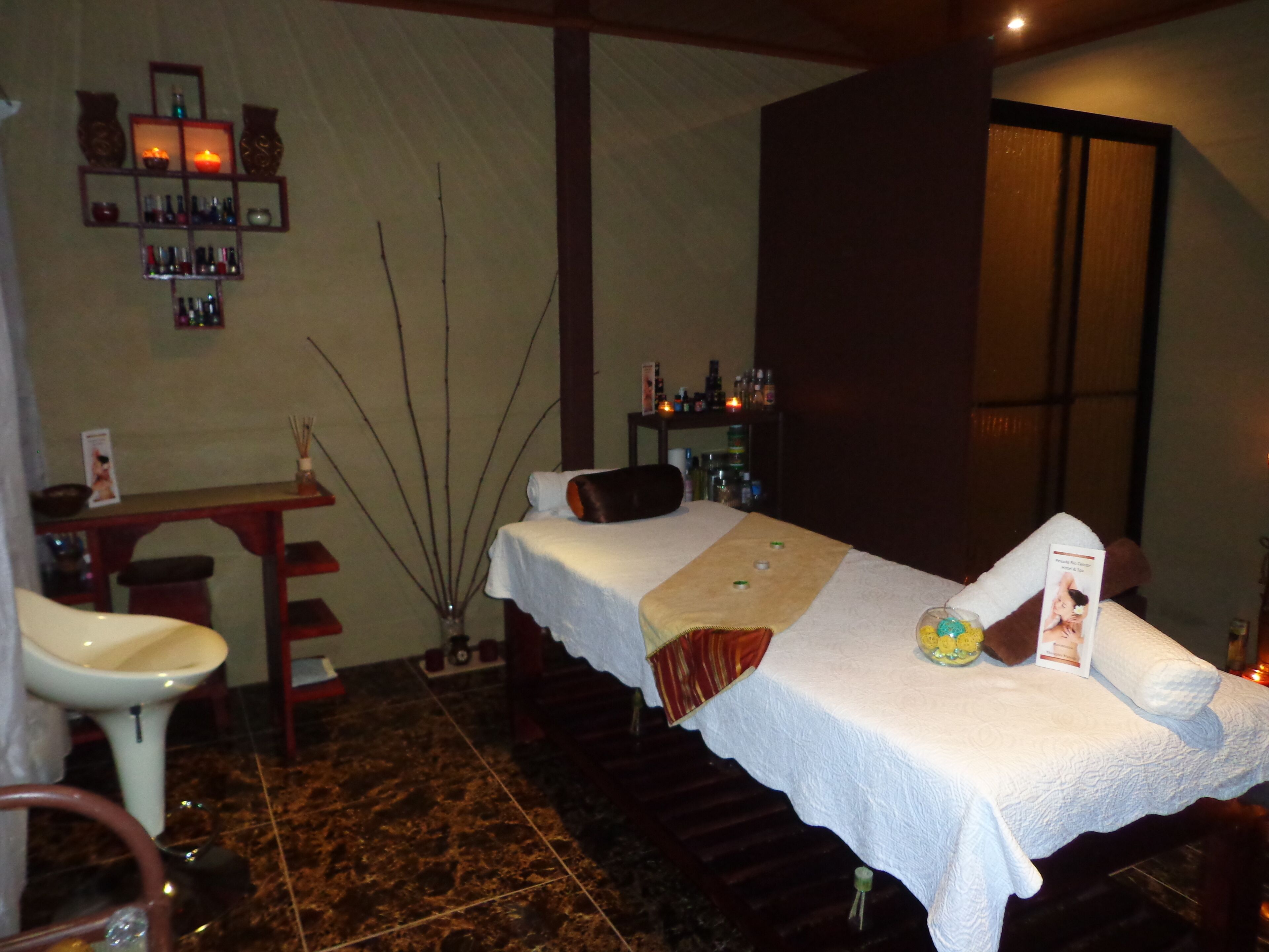 Une salle de spa équipée d’une table de massage, d’un lavabo et d’étagères remplies de bouteilles.