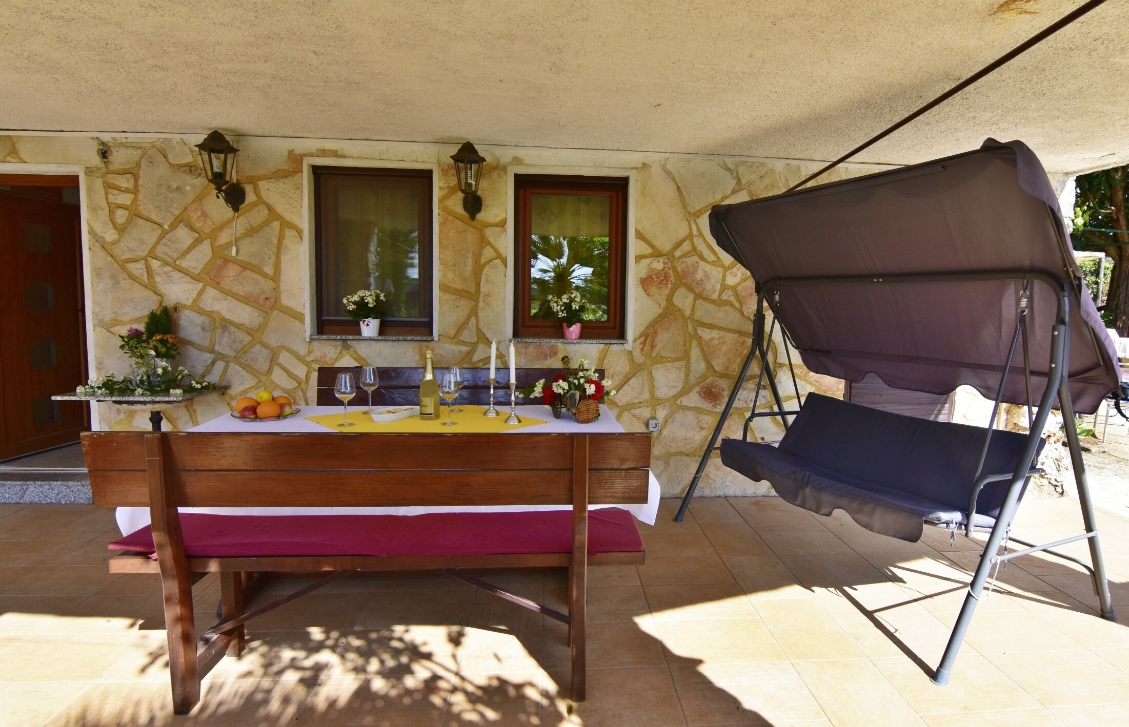Un área de comedor al aire libre con una mesa de madera para dos personas, un banco acolchado y una pérgola.