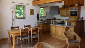 Une cuisine avec des meubles de rangement en bois, une table à manger avec des chaises et un fauteuil en osier.