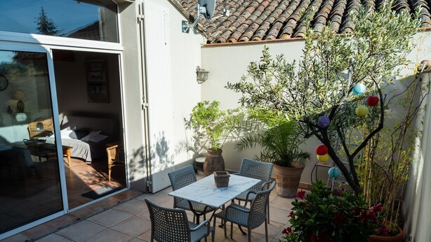Un espace patio aménagé avec une table et des chaises, un pot de fleurs et une porte-fenêtre coulissante donnant sur un espace intérieur.