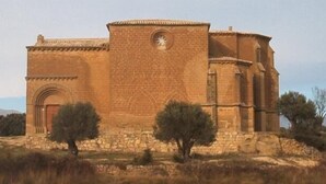 Un bâtiment en pierre doté d’une tour arrondie et de fenêtres en arc de cercle, entouré de pelouse et d’arbres.