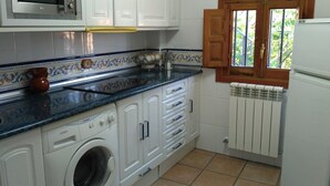 Une cuisine compacte avec des meubles blancs, un lave-linge, un four à micro-ondes et une fenêtre dotée de volets en bois.