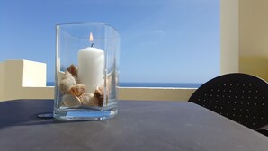 A glass candle holder with a lit candle and seashells on a table with a view of the ocean. - Costa Calma Penthause. Wonderful penthouse On one of the best beaches in Europe (Pájara)