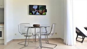 A dining area with a glass table and chairs, a television mounted on the wall, and a kitchen in the background. - Costa Calma Penthause. Wonderful penthouse On one of the best beaches in Europe (Pájara)
