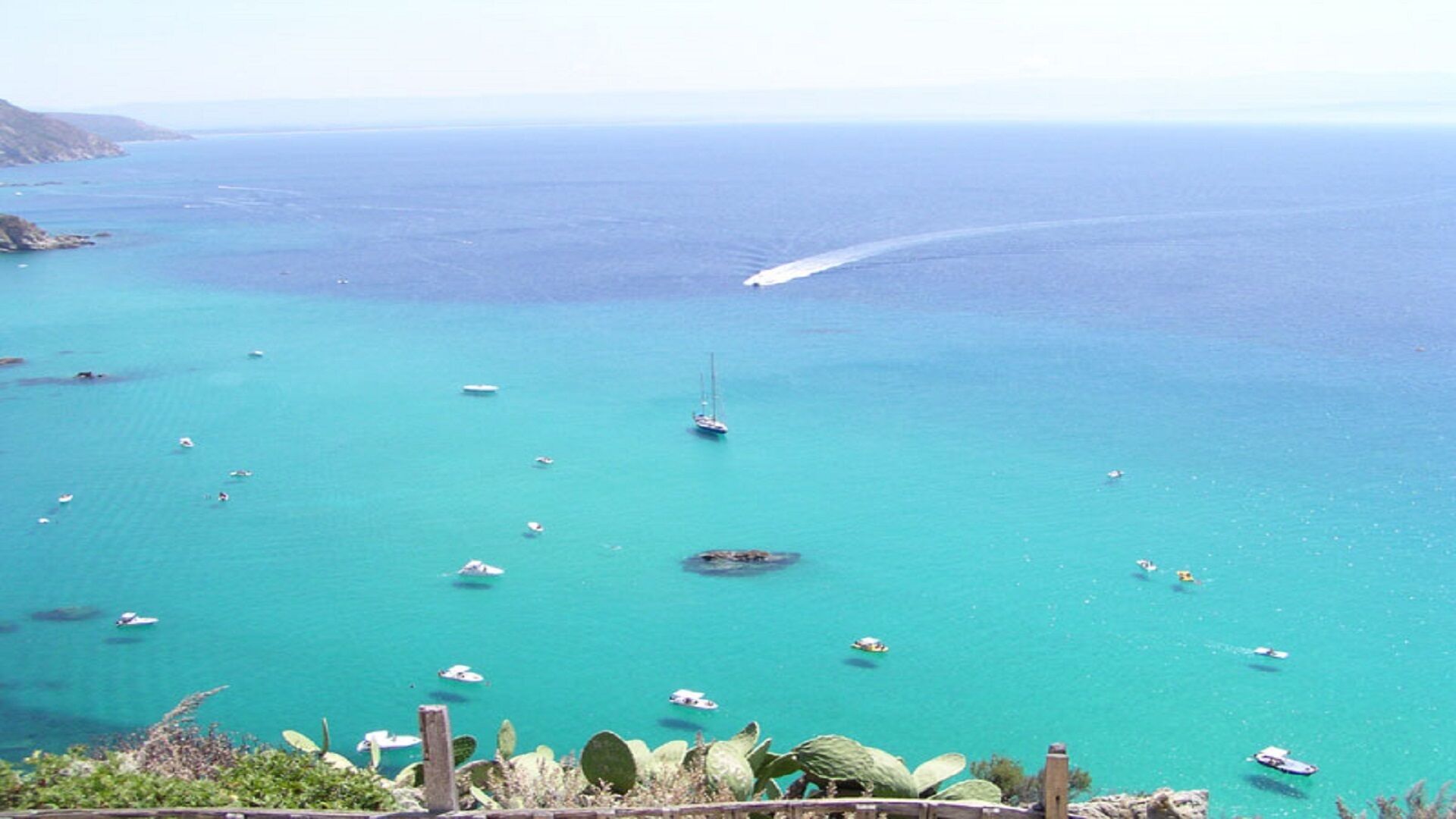 Paesaggio costiero con barche e acqua turchese cristallina.